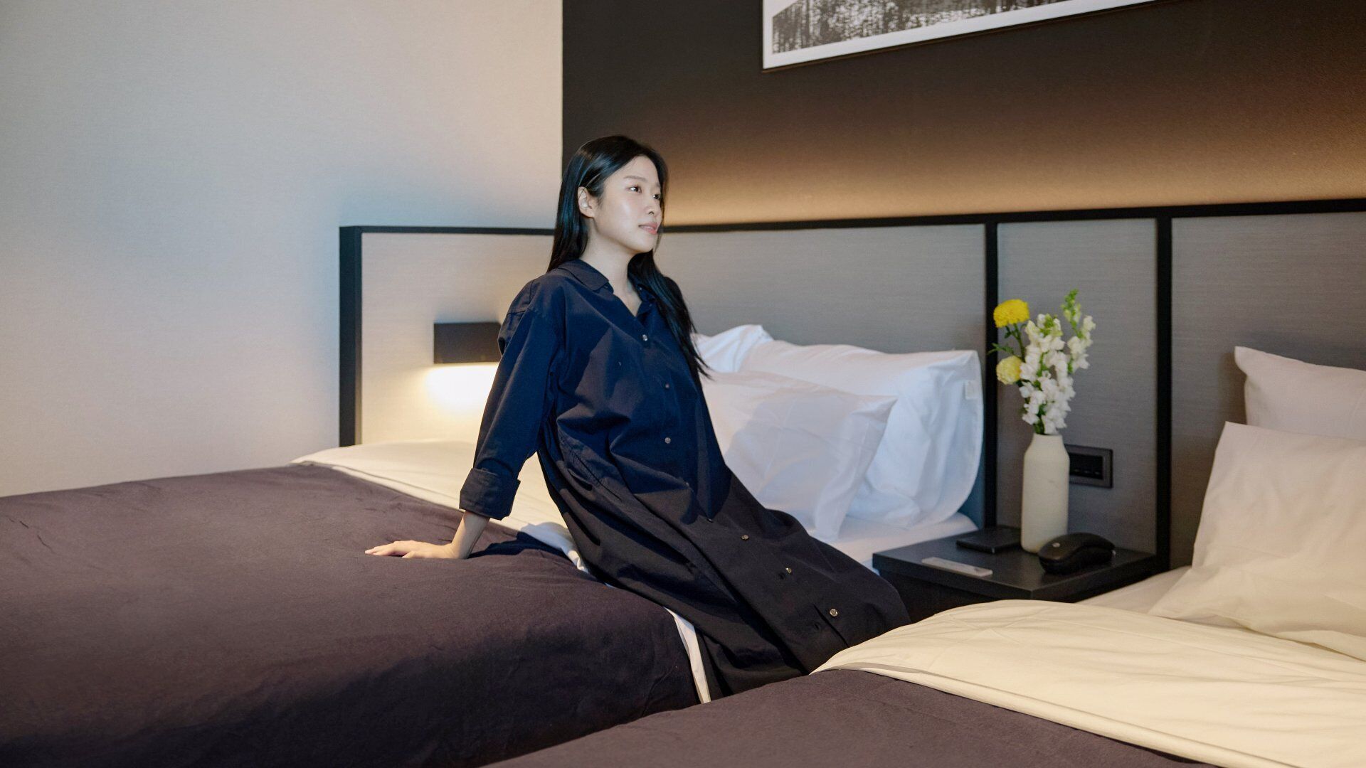 A hotel room with a bed, a nightstand, and a vase with flowers.