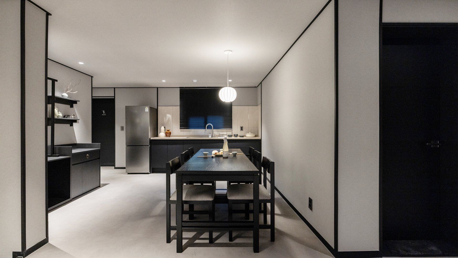 A modern kitchen with a dining area, featuring a dark wooden table and chairs, a built-in oven, and a pendant light.