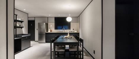 A modern kitchen with a dining area, featuring a dark wooden table and chairs, a built-in oven, and a pendant light.