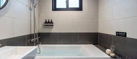 Un baño moderno con bañera, ducha y lavamanos. Hay una ventana sobre la bañera y un letrero de precaución en la pared.