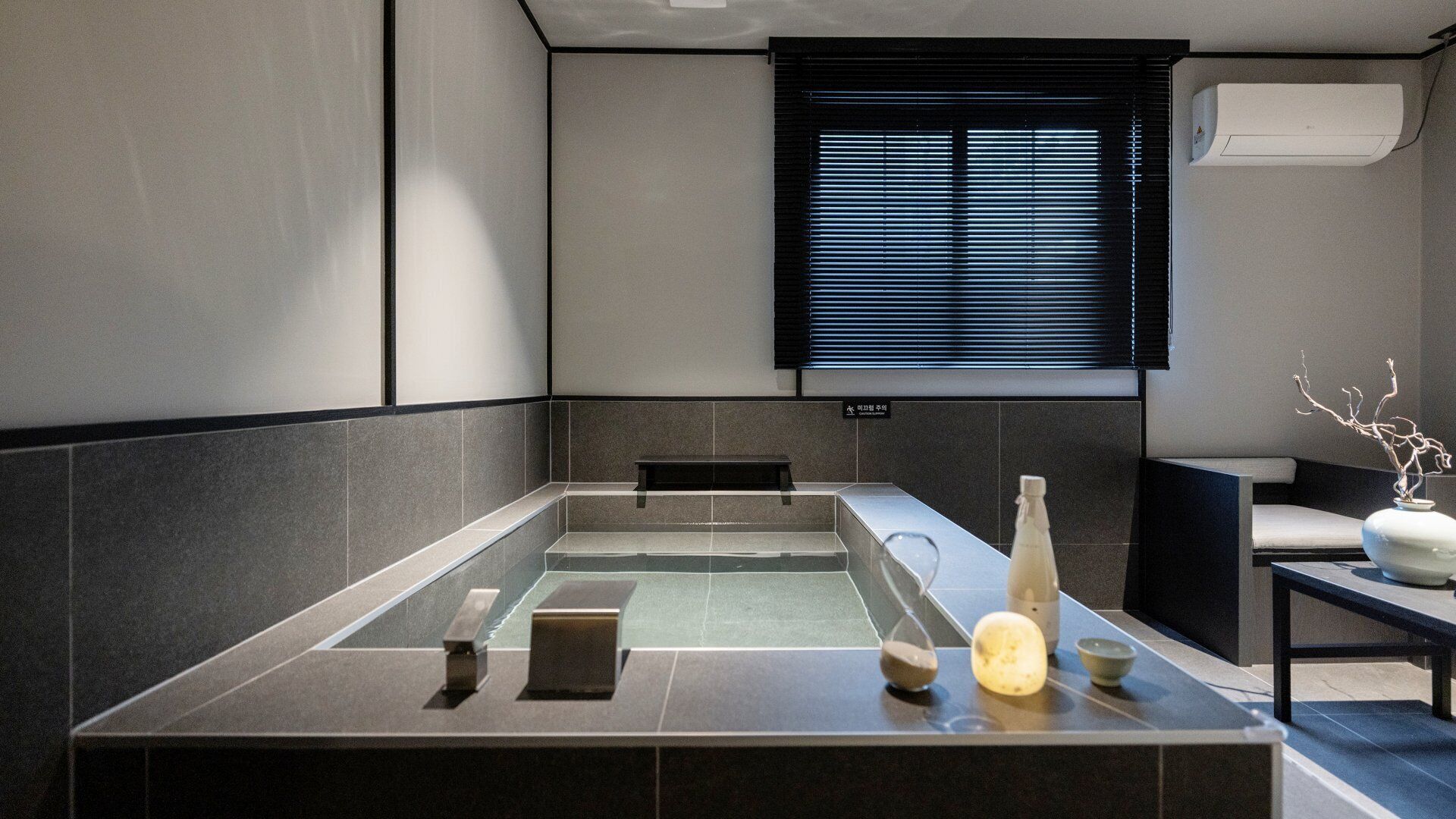Una moderna sala spa con vasca idromassaggio, una panca e un tavolino con oggetti decorativi.