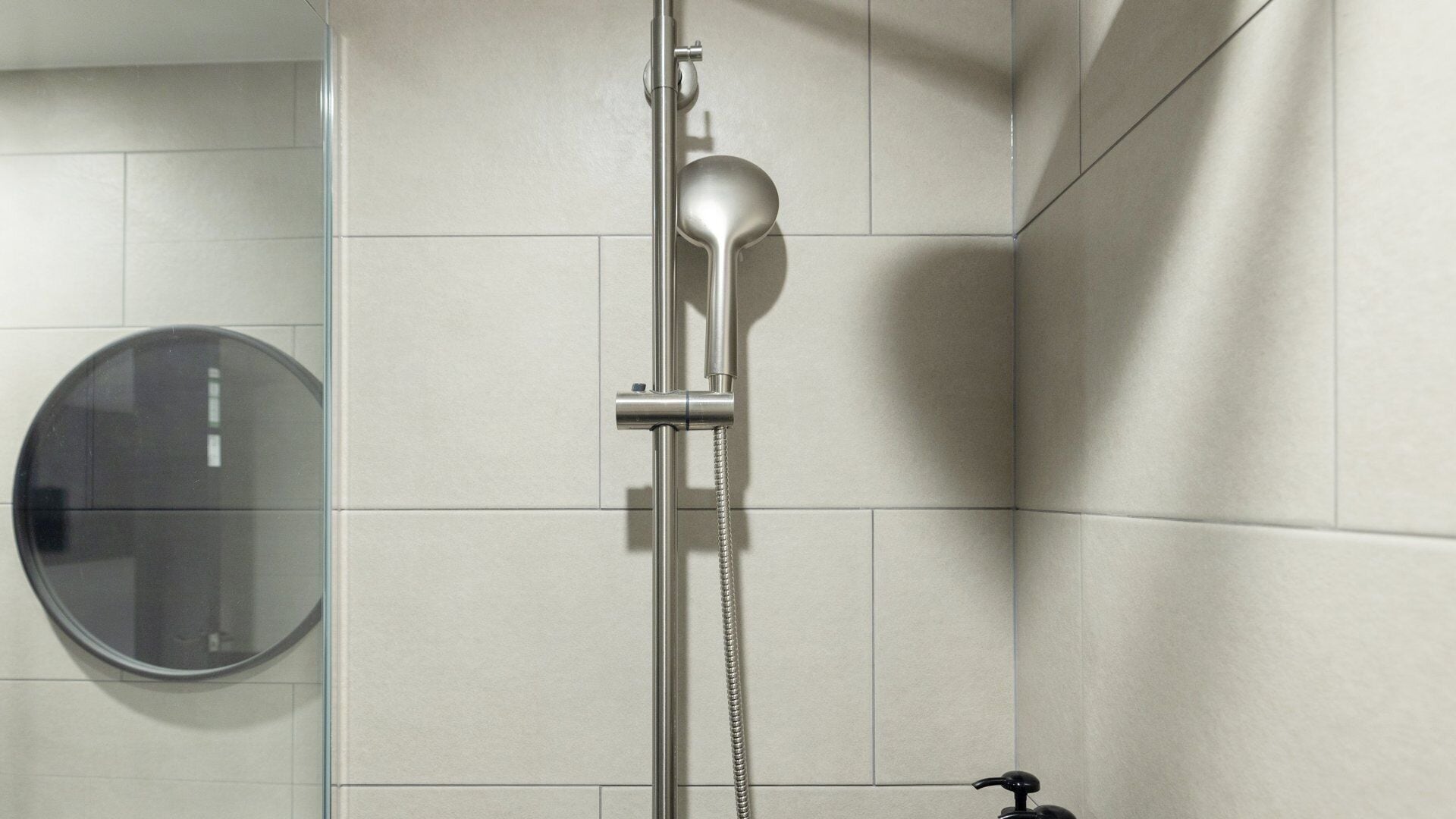 Un baño moderno con ducha, un espejo redondo y un dispensador de jabón.
