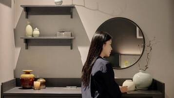 A person standing in a room with a modern interior design, including a black shelf with decorative items and a round mirror on the wall.