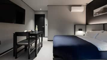 Habitación de hotel moderna con cama, escritorio y silla. Tiene aire acondicionado de pared y un cuadro enmarcado sobre la cama.