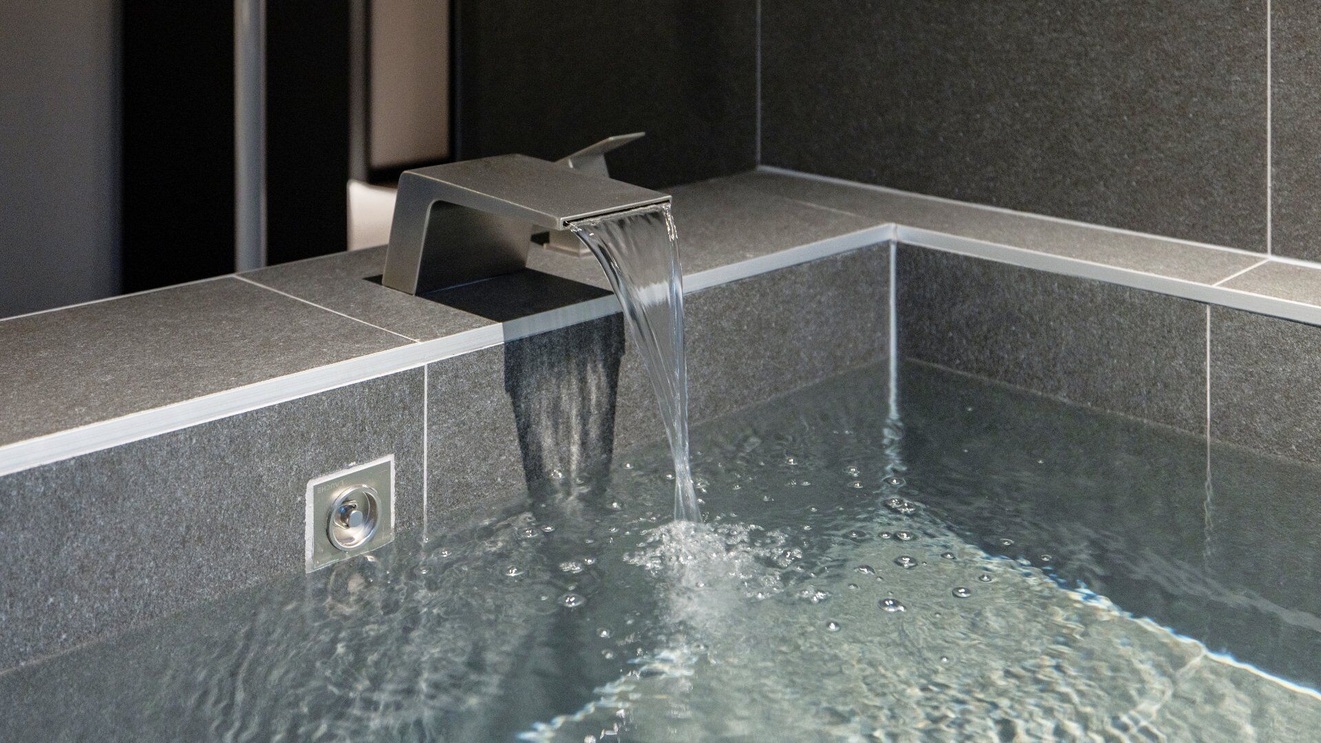 A modern bathroom with a built-in bathtub, a faucet, and a control panel.