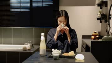 A person seated at a table with a teapot, a bottle, and a plate of food.