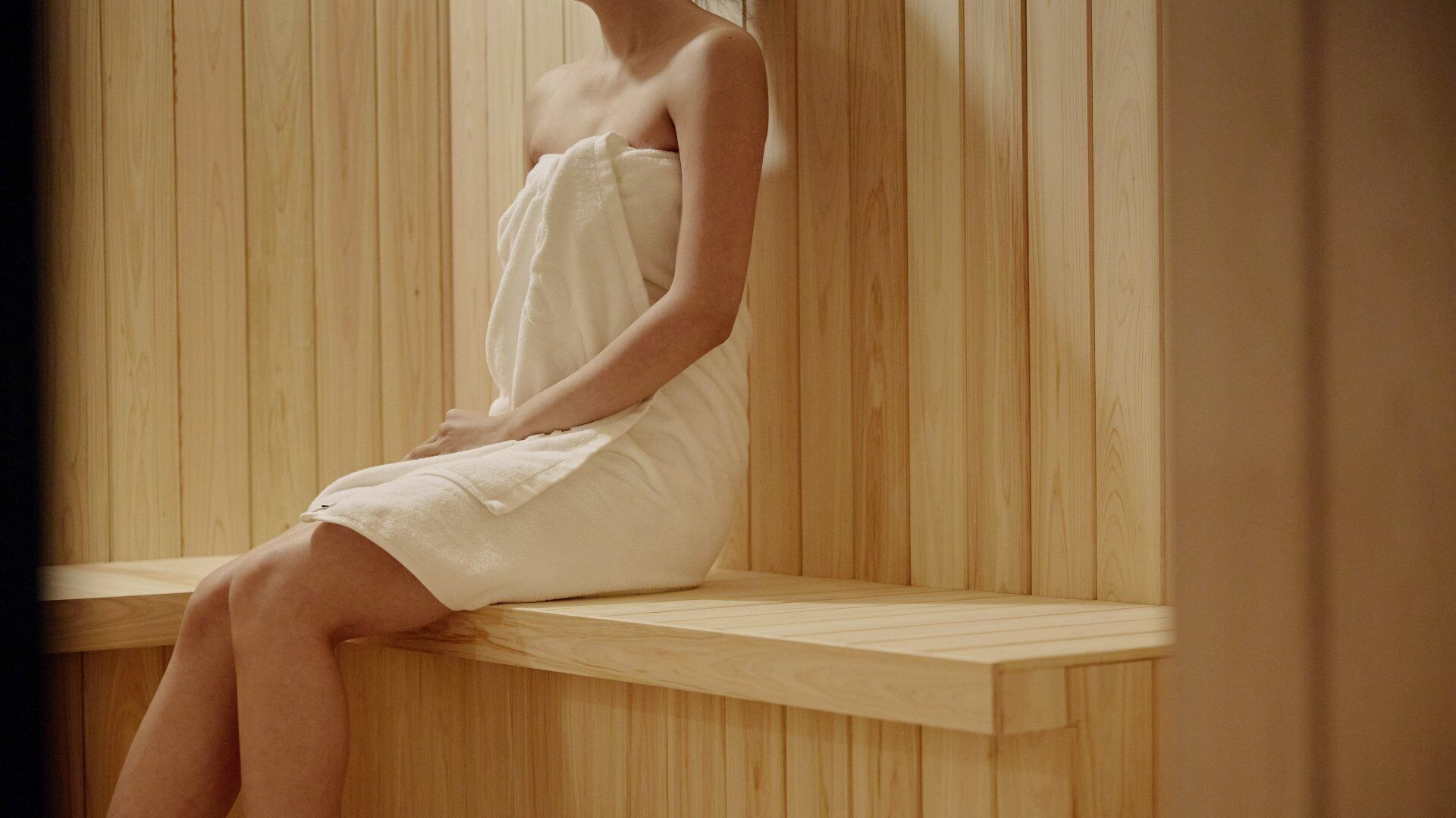 Una persona sentada en un banco de madera en una habitación con paneles de madera verticales.