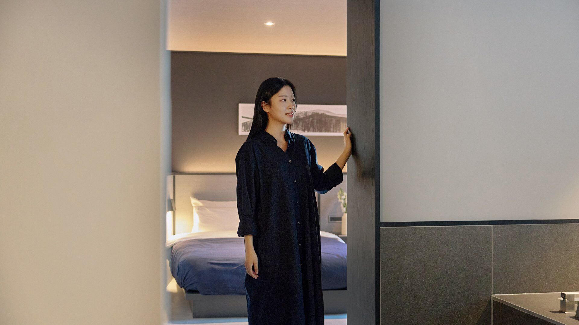 A modern hotel room with a bed, a nightstand, and a wall-mounted shelf.