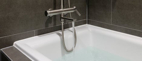 A modern bathroom with a white bathtub, chrome fixtures, and grey tiled walls.