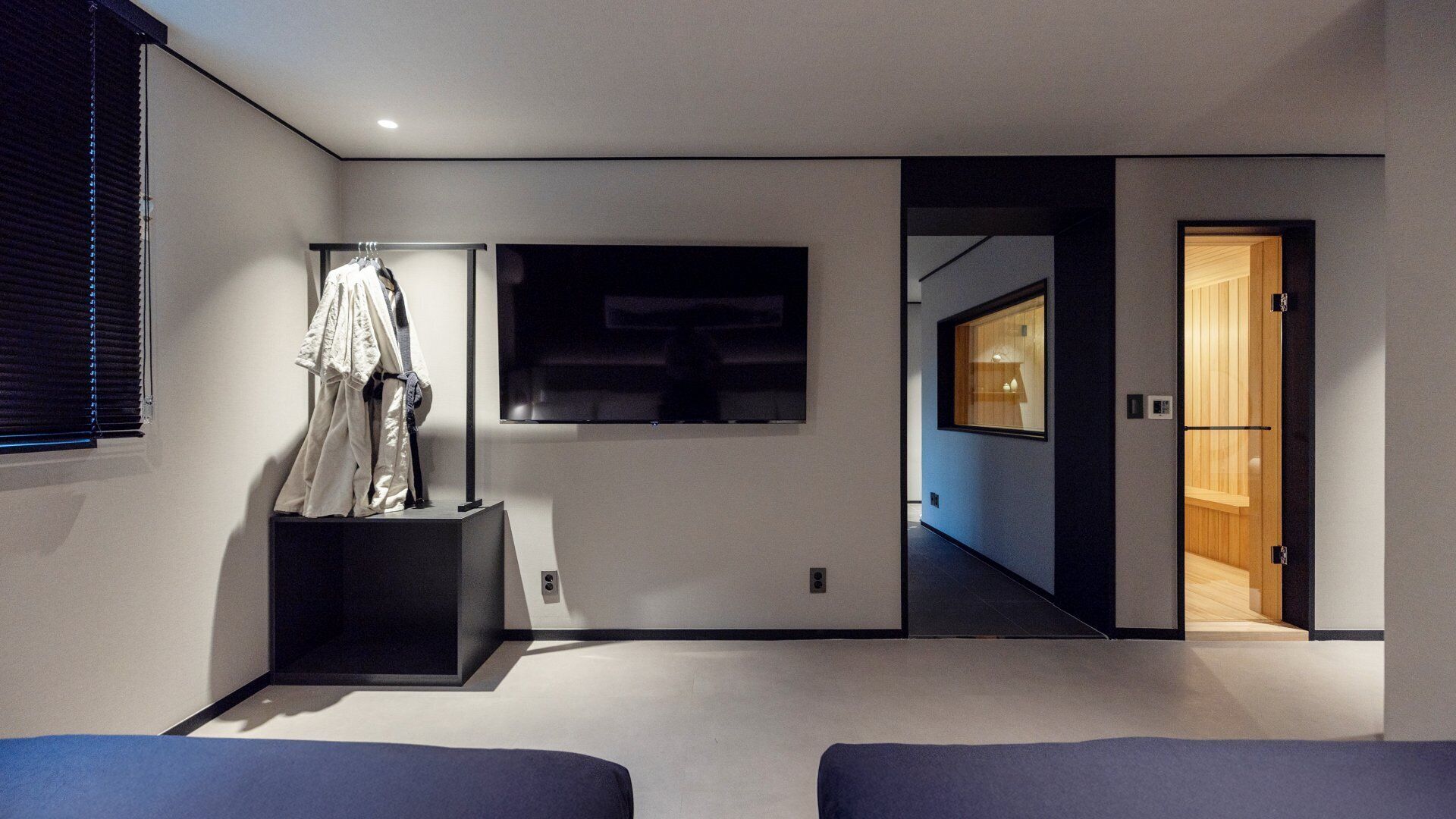 A modern living room with a flat-screen TV mounted on the wall, a clothing rack, and a wooden door leading to another room.
