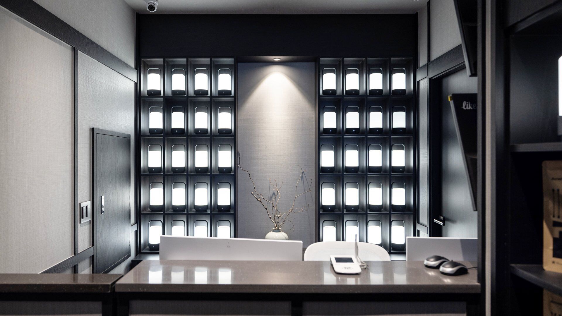 A modern office space with a desk, chairs, a vase with branches, and a wall with multiple illuminated panels.