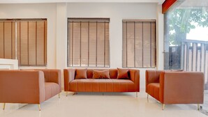 A modern living room with a brown leather sofa, two armchairs, and large windows with blinds. - The Byke Boutique Tejjora (Lucknow)