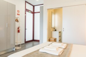 Ein Hotelzimmer mit einem Bett, einem Kleiderschrank, einem Spiegel, einem kleinen Hocker und einem Feuerlöscher.