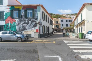 Une rue bordée d’immeubles, ornée d’une fresque murale, avec des voitures garées et un passage piéton.