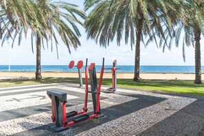 Draußen aufgestellte Trainingsgeräte, Palmen und Blick auf den Strand.