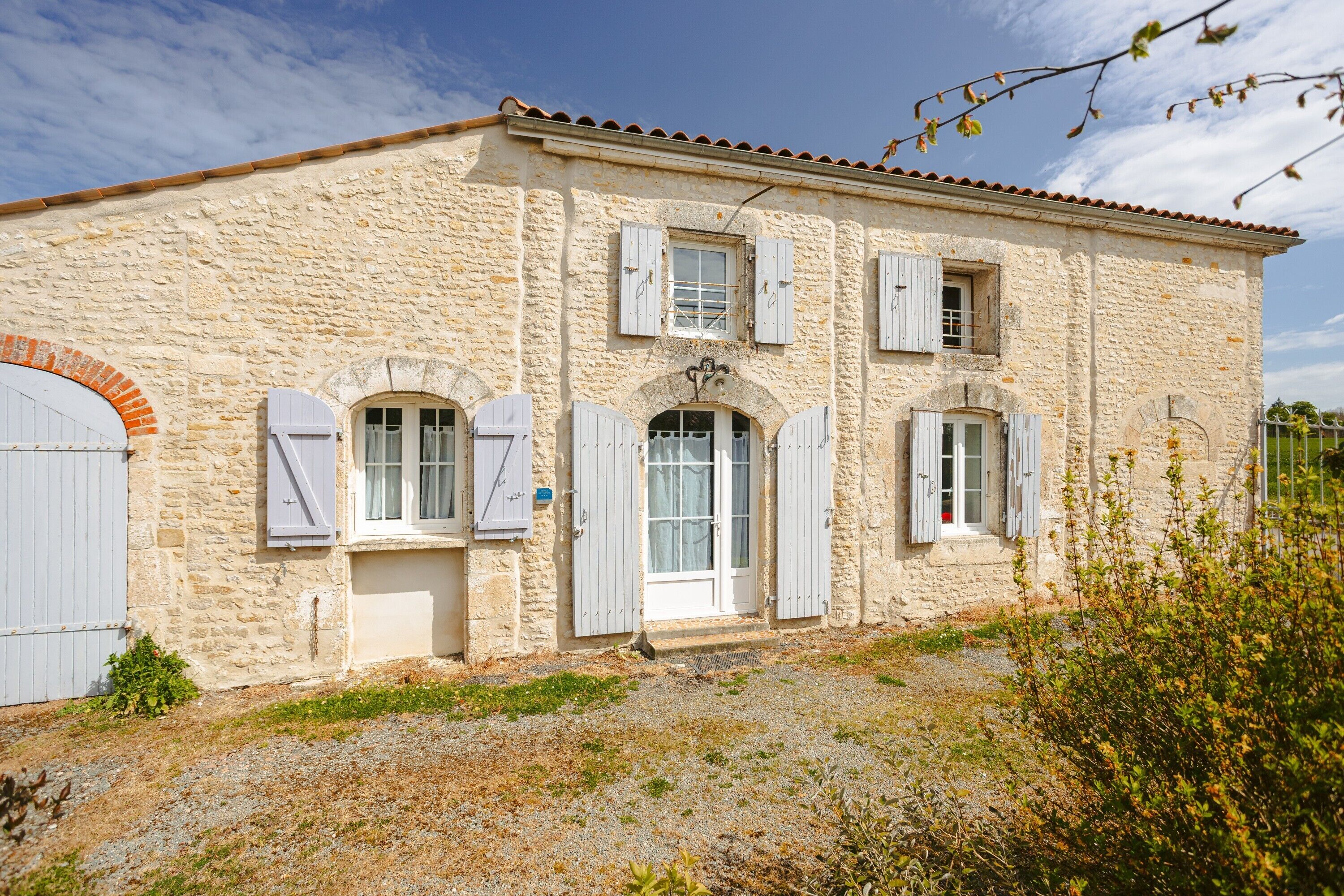 A stone building with arched doorways, a tiled roof, and white shutters.