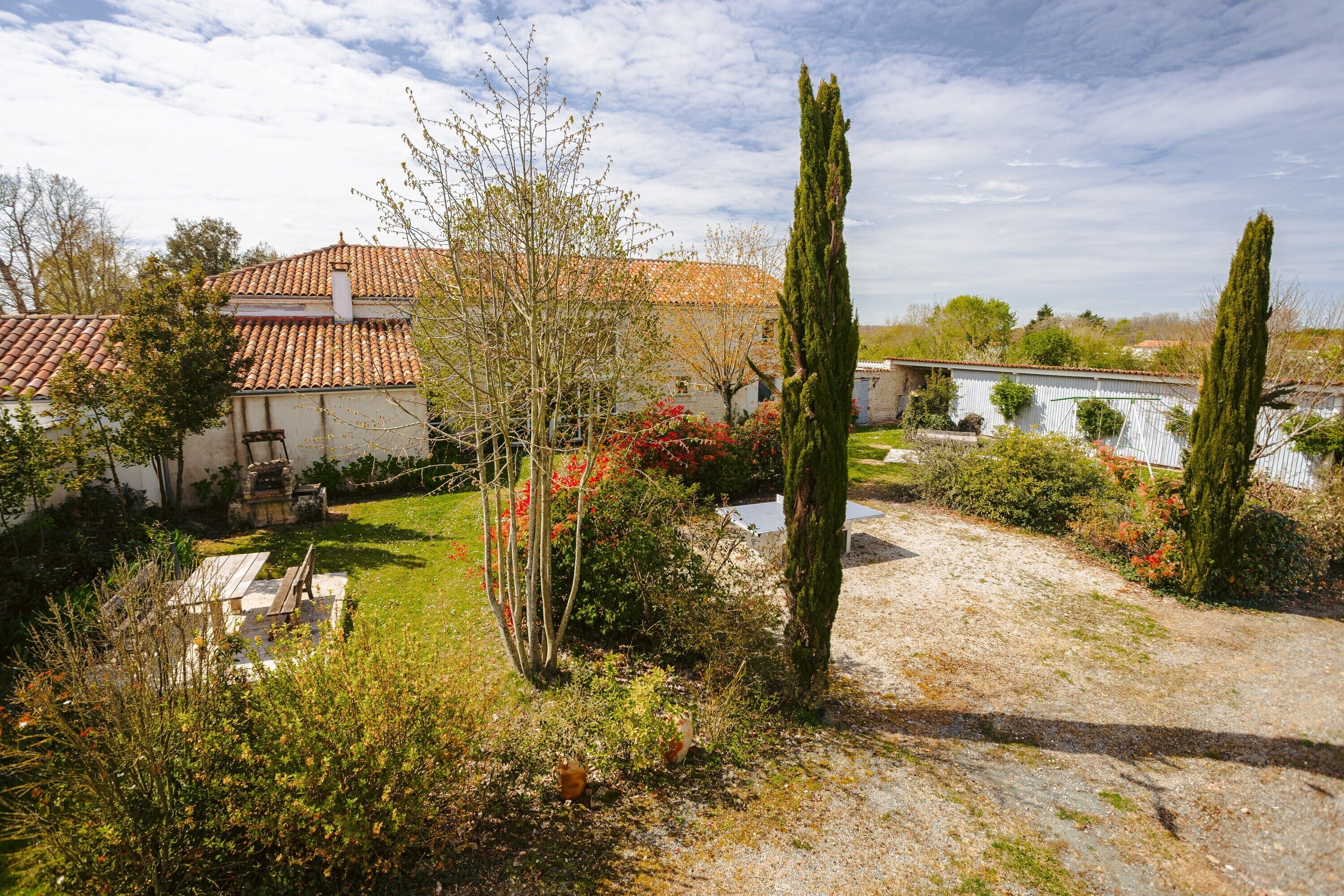 Une maison avec un toit en tuiles, un jardin avec différentes espèces de plantes et un chemin de gravier.