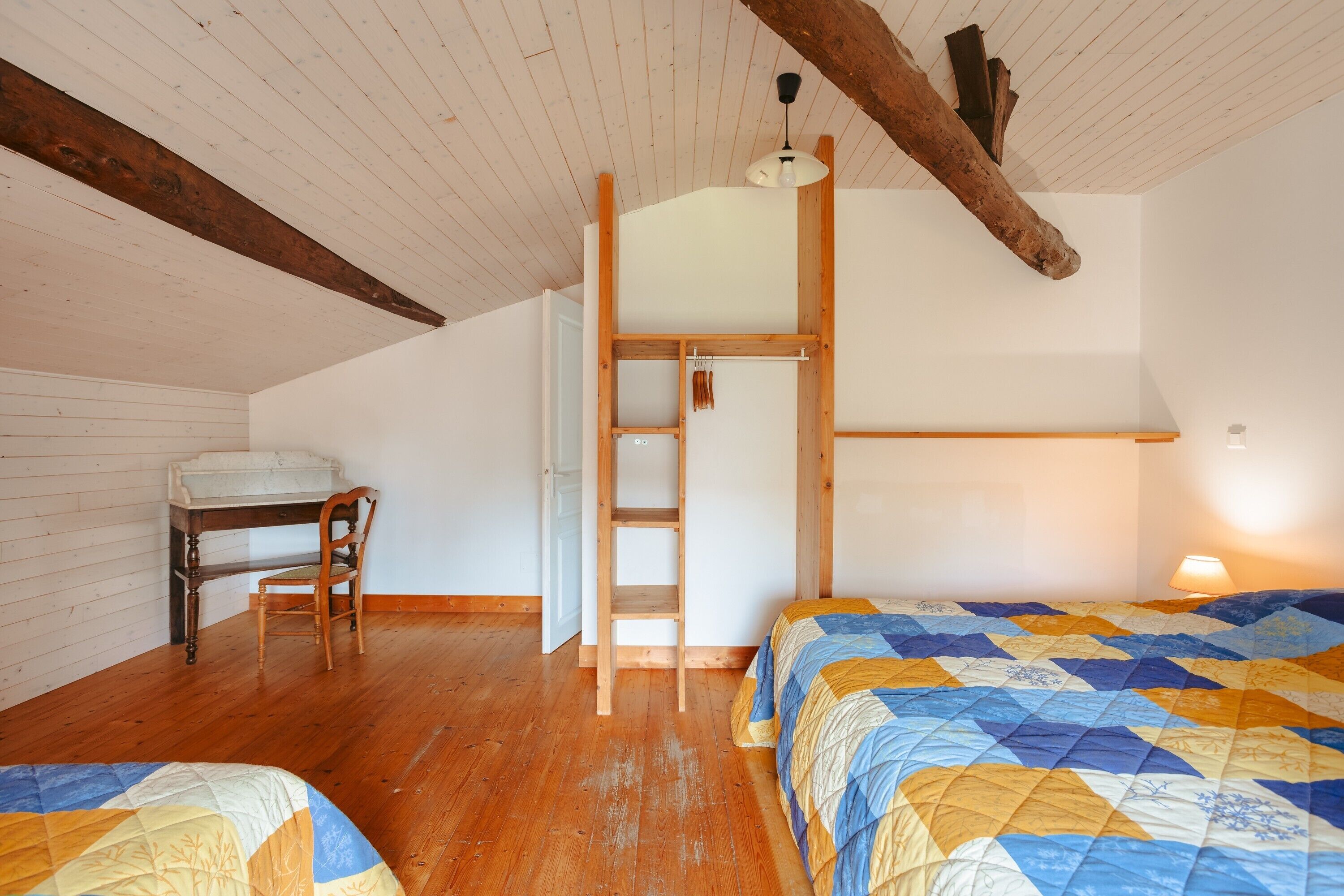 Une chambre avec deux lits, un bureau, une chaise, une échelle et une poutre en bois au plafond.