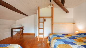 A bedroom with two beds, a desk, a chair, a ladder, and a wooden ceiling beam.