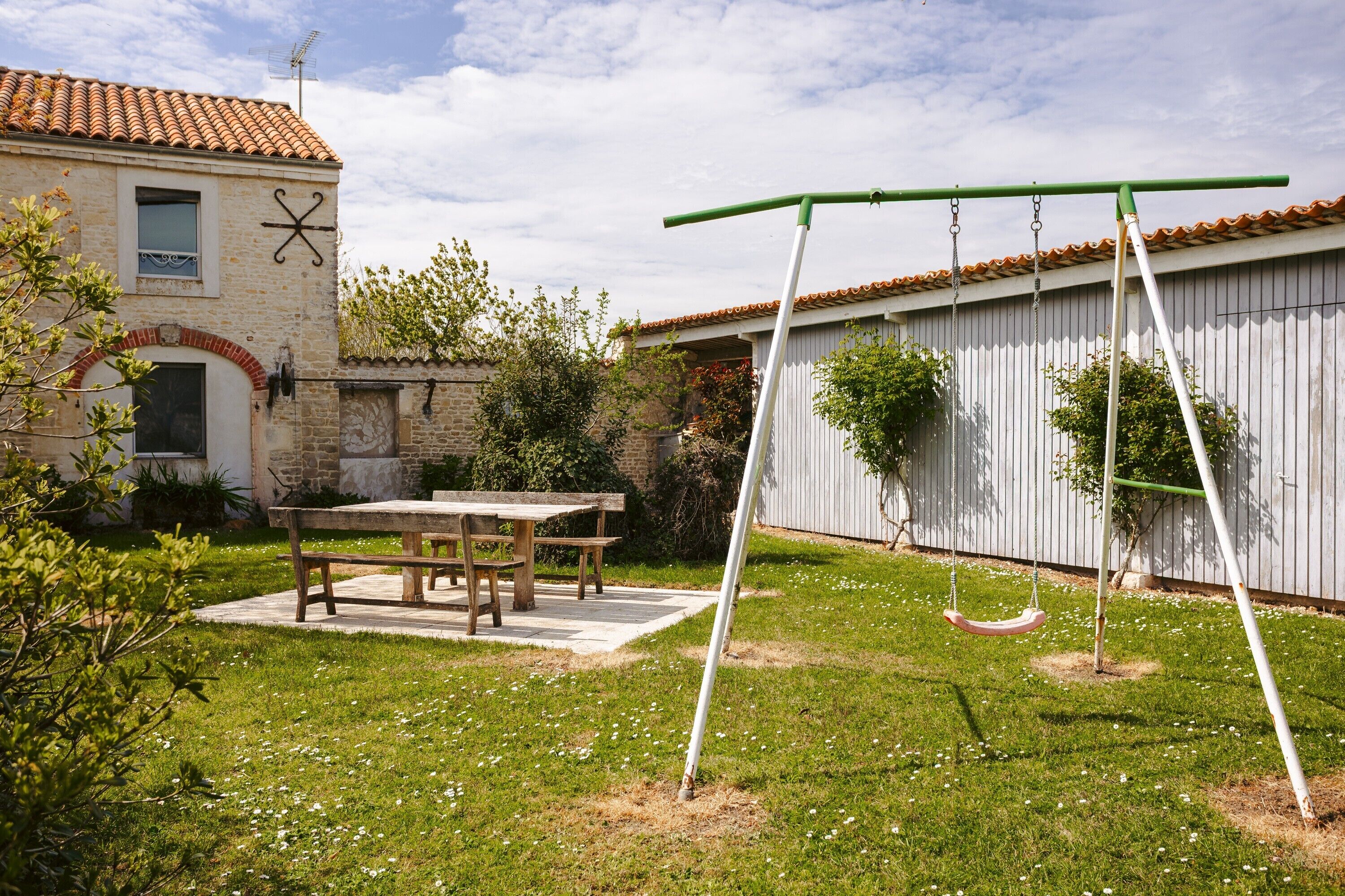 A patio with a table and chairs, a swing set, and a building with a tiled roof.