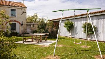 A patio with a table and chairs, a swing set, and a building with a tiled roof.