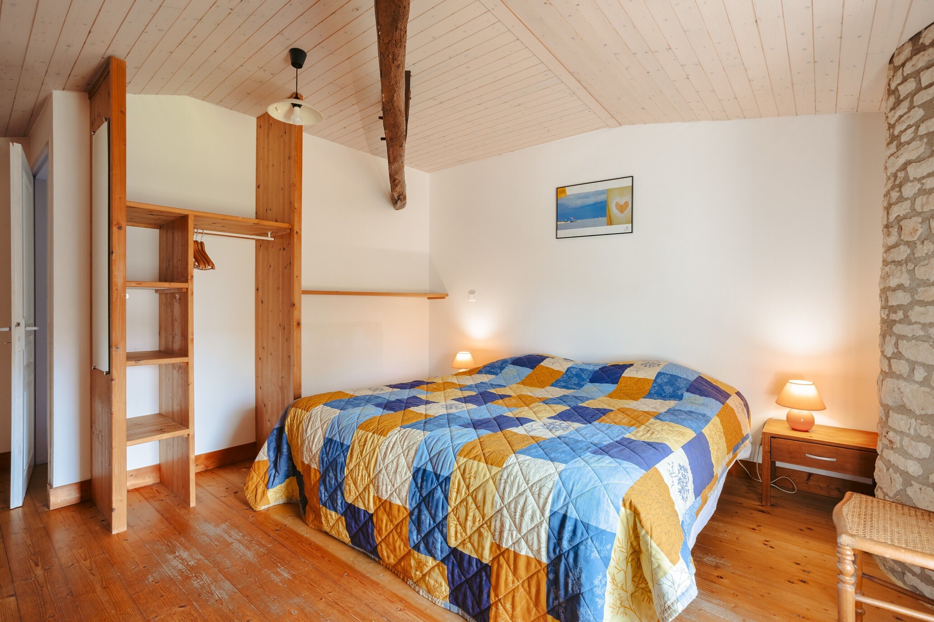 Une chambre avec une échelle en bois, un lit recouvert d’une courtepointe, une table de chevet et une lampe.