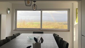 Zona pranzo con un tavolo grande, sedie e vista su un paesaggio rurale attraverso un'ampia finestra.