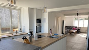 Una cucina moderna con un'isola centrale, un'area pranzo con tavolo grigio e un soggiorno con divano e tavolino grigio.