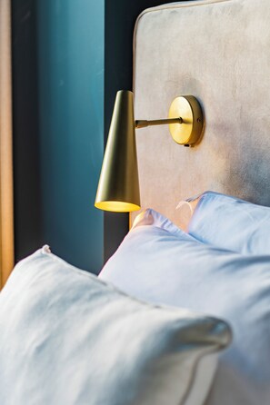 Una cama con cabecera, una lámpara de pared y una ventana con vistas.