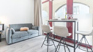 A modern room with a grey sofa, two bar stools, a table with wine glasses, and a large window with red framing. - Santa Cruz Studio 2 by Atlantic Holiday (Santa Cruz)