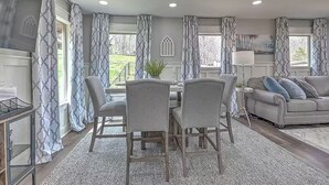 Een moderne woonkamer met een grijze bank, een eettafel met stoelen en behang met een patroon.
