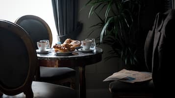 A dining table with croissants, coffee cups, and a menu. There are chairs around the table, and a plant is in the background.