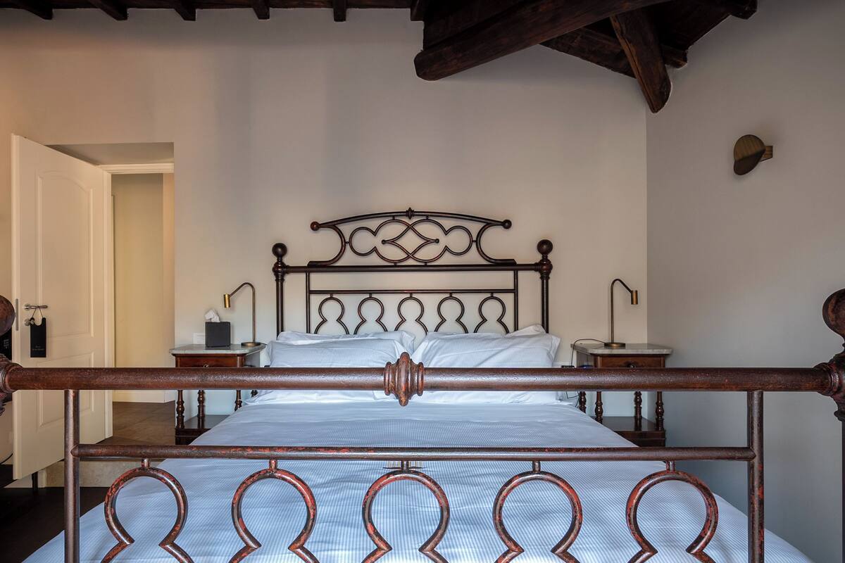A bedroom with a wooden ceiling, a metal bed frame, two bedside tables, and a white door.
