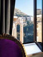 Una habitación con un amplio ventanal que da a un paisaje urbano, con ruinas antiguas y edificios modernos.
