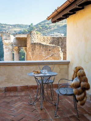 A terrace with a table and chairs, a view of ancient ruins, and a fluffy dog. - Locanda Sibilla Luxury Suites (Tivoli)
