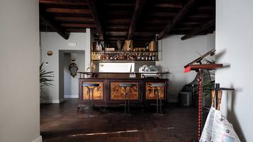 A bar area with a wooden bar counter, stools, and a shelf with bottles.