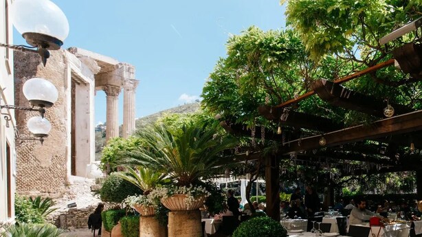 Un patio con mesas al aire libre, plantas en macetas y arquitectura clásica.