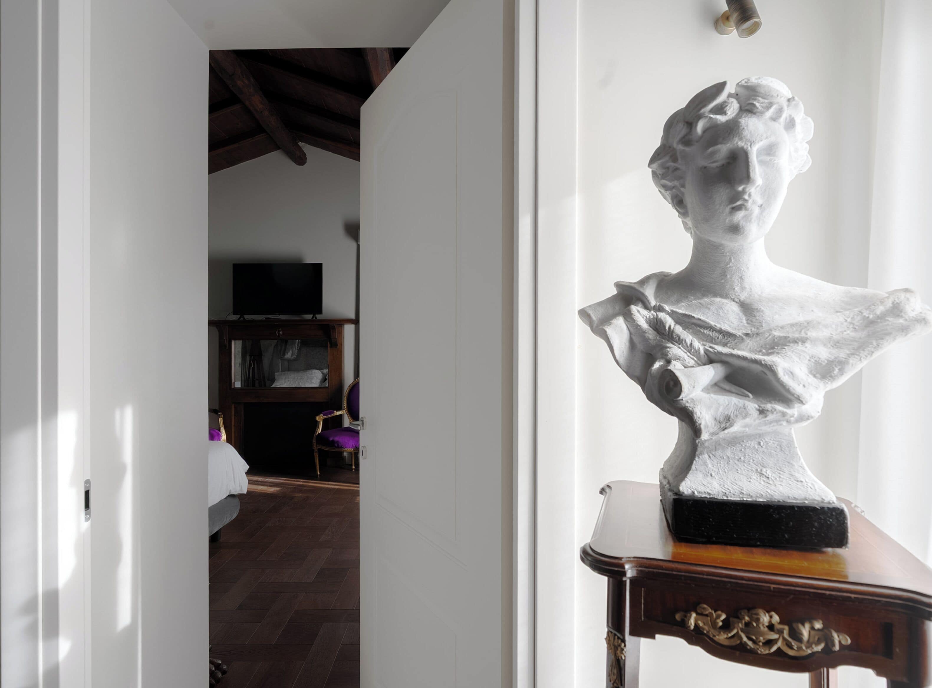 Una habitació amb terra de fusta, paret blanca i una escultura de bust sobre una taula.