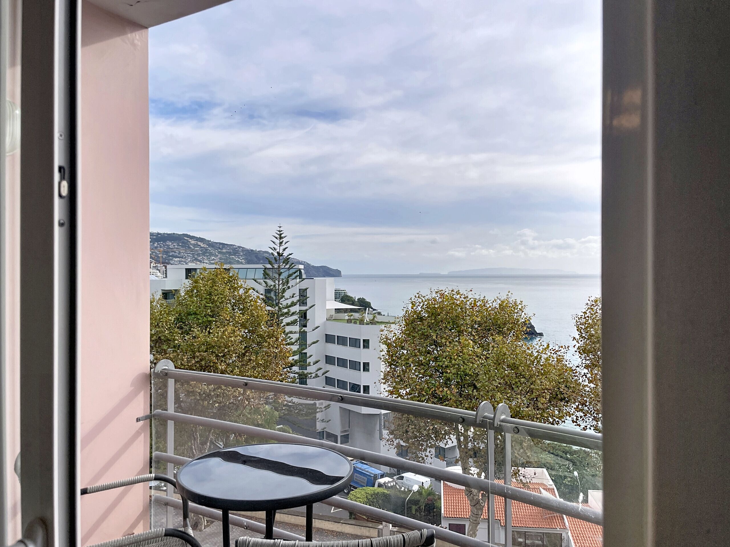 A balcony with a table and chairs, overlooking a cityscape and a body of water.