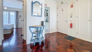 Ein Hotelgang mit Holzboden, einem blauen Konsolentisch, einem Spiegel und einer Tür mit Feuerlöscher.