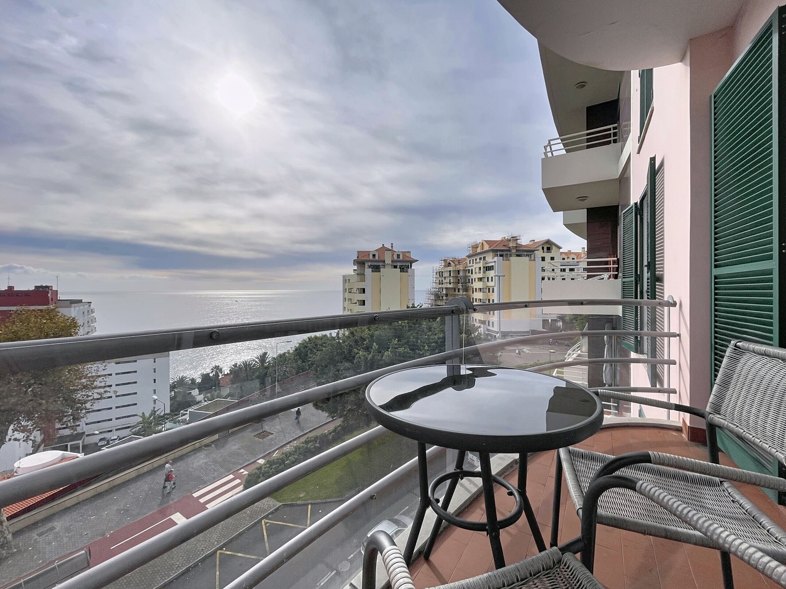 A balcony with a table and chairs, overlooking a cityscape and the sea.