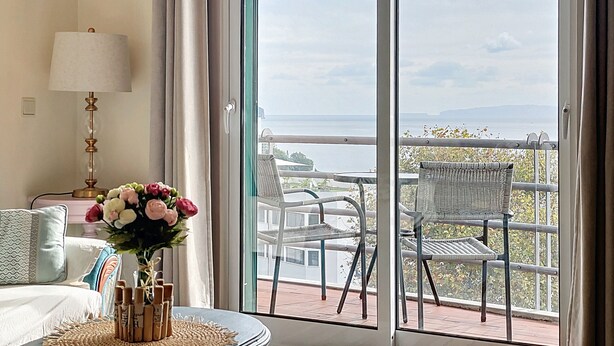 Ein Hotelzimmer mit Balkon, einem Bett, einer Lampe und einer Blumenvase.