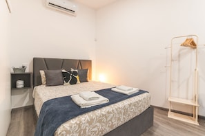 A bedroom with a bed, pillows, a bedside table, a hanging clothes rack, and an air conditioning unit. - Santa Cruz Studio 3 by Atlantic Holiday (Santa Cruz)