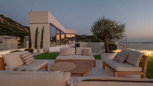 A modern outdoor seating area with sofas and a coffee table, overlooking a body of water and hills. - Spacious 5-bedroom penthouse in gorgeous Rafailovići - Budva (Rafailovići)