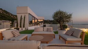 A modern outdoor seating area with sofas and a coffee table, overlooking a body of water and hills. - Spacious 5-bedroom penthouse in gorgeous Rafailovići - Budva (Rafailovići)