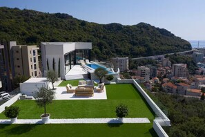 A modern hotel with a rooftop pool, a well-maintained lawn, and a view of the city and hills in the background. - Spacious 5-bedroom penthouse in gorgeous Rafailovići - Budva (Rafailovići)