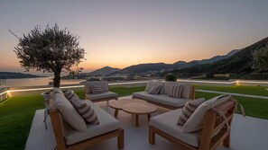 An outdoor seating area with sofas and a round table, overlooking a body of water and hills. - Spacious 5-bedroom penthouse in gorgeous Rafailovići - Budva (Rafailovići)