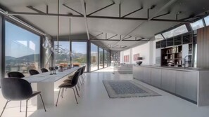 A modern kitchen with a large island, a dining area with chairs, and a view of the city through large windows. - Spacious 5-bedroom penthouse in gorgeous Rafailovići - Budva (Rafailovići)