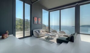 A modern living room with large windows, a sofa, a coffee table, and a rug. - Spacious 5-bedroom penthouse in gorgeous Rafailovići - Budva (Rafailovići)