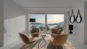 A modern living room with a large window, two chairs, a small table, and a lamp. - Spacious 5-bedroom penthouse in gorgeous Rafailovići - Budva (Rafailovići)